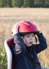 Child in red helmet sitting on the bike seat for baby with a wheat field in the background.Portrait with copy space.