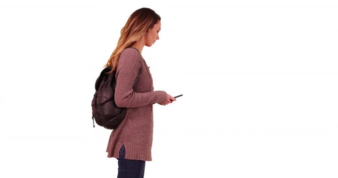 Female millennial answering text message on smartphone, waiting for someone on white background with copyspace. Young Caucasian woman with backpack responding to text in studio with copy space. 4k