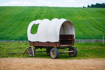 Old covered wagon with white top against green grass field background.