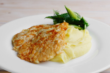 Plate with chopped pork in breading and mashed potato decorated with cucumber
