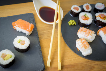 Sushi on a wooden table on black slate plate with soy sauce and chopsticks