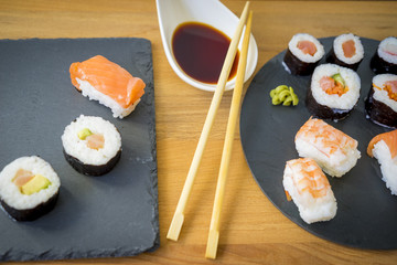 Sushi on a wooden table on black slate plate with soy sauce and chopsticks