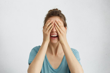 Happy woman closing her eyes with hands going to see surprise prepared by her husband standing and smiling in anticipation for something wonderful. Young cheerful lady covering her face with hands