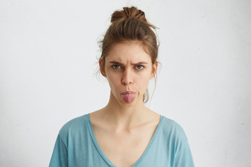 Angry young female showing her digust and distaste having gloomy expression demonstaring tongue refusing to do something. Furious beautiful woman with upset look rejecting her guilt isolated on white
