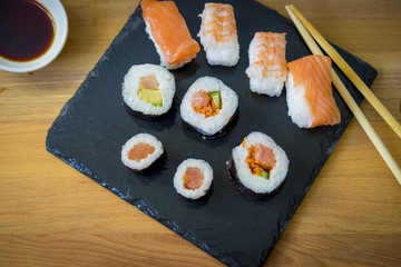 Sushi on a wooden table on black slate plate with soy sauce and chopsticks