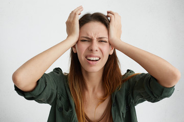 Frustrated woman having terrible headache keeping hands on head frowning her face with pain looking unhappy and stressful. Housewife in despair having stressful situation in her life suffering