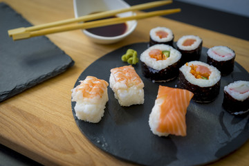 Sushi on a wooden table on black slate plate with soy sauce and chopsticks