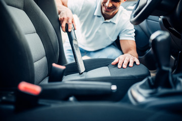 Man cleans car interior with vacuum cleaner - obrazy, fototapety, plakaty