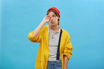 Beautiful female rubbing her eyes looking tired after go fishing with her husband for all night wanting to sleep isolated on blue background. Woman dressed casually having sleepless expression © WHstudio Leushin N