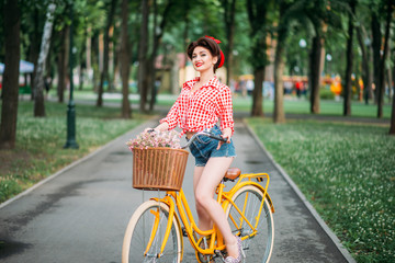 Pinup girl on retro bicycle with backet of flowers