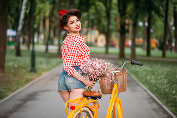 Pinup girl on retro bicycle with backet of flowers