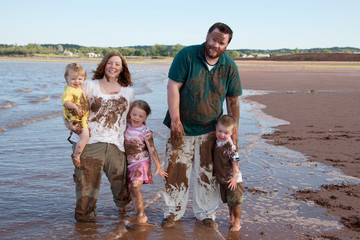 Parents playing on beach with three muddy young children. 