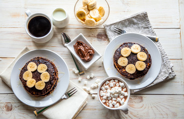 Breakfast for couple included oat pancakes with banana, nutella, honey, with coffe and milk and cacao with marshmallow on white wooden  background