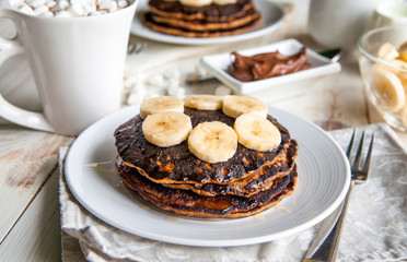 Breakfast for couple included oat pancakes with banana, nutella, honey, with coffe and milk and cacao with marshmallow on white wooden  background