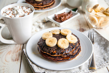 Breakfast for couple included oat pancakes with banana, nutella, honey, with coffe and milk and cacao with marshmallow on white wooden  background