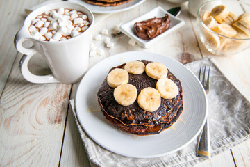 Breakfast for couple included oat pancakes with banana, nutella, honey, with coffe and milk and cacao with marshmallow on white wooden  background