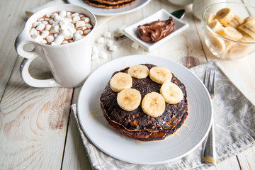 Breakfast for couple included oat pancakes with banana, nutella, honey, with coffe and milk and cacao with marshmallow on white wooden  background