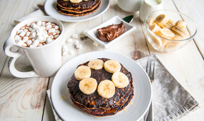 Breakfast for couple included oat pancakes with banana, nutella, honey, with coffe and milk and cacao with marshmallow on white wooden  background