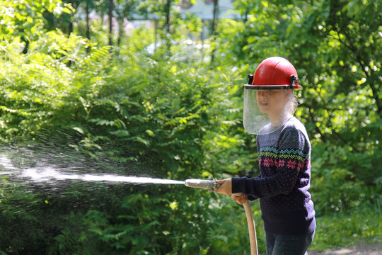 Teenager learning the firefighter profession. The girl in fire helmet pours water from the hose. Educational program for kids
