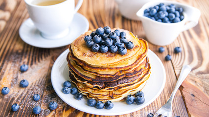 Pancakes healthy breakfast with blueberries, bog whortleberry, cup of green tea, cup of blueberries and teapot on brown wooden background 