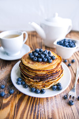 Pancakes healthy breakfast with blueberries, bog whortleberry, cup of green tea, cup of blueberries and teapot on brown wooden background 