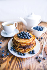 Pancakes healthy breakfast with blueberries, bog whortleberry, cup of green tea, cup of blueberries and teapot on brown wooden background 