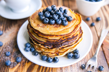 Pancakes healthy breakfast with blueberries, bog whortleberry, cup of green tea, cup of blueberries and teapot on brown wooden background 