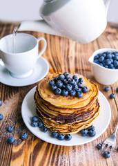 Pancakes healthy breakfast with blueberries, bog whortleberry, cup of green tea, cup of blueberries and teapot on brown wooden background 