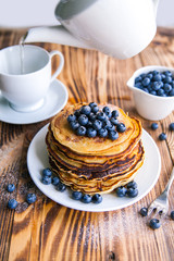 Pancakes healthy breakfast with blueberries, bog whortleberry, cup of green tea, cup of blueberries and teapot on brown wooden background 