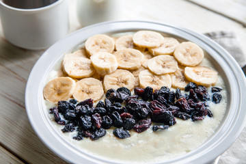 Fitness diet healthy Breakfast which included oatmeal oat porridge with milk, banana and  raisins without sugar and fat with cup of coffee with milk on the white wooden background 