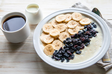Fitness diet healthy Breakfast which included oatmeal oat porridge with milk, banana and  raisins without sugar and fat with cup of coffee with milk on the white wooden background 