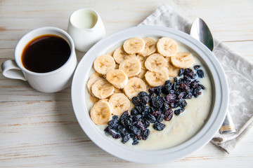 Fitness diet healthy Breakfast which included oatmeal oat porridge with milk, banana and  raisins without sugar and fat with cup of coffee with milk on the white wooden background 