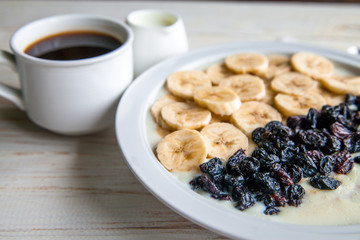 Fitness diet healthy Breakfast which included oatmeal oat porridge with milk, banana and  raisins without sugar and fat with cup of coffee with milk on the white wooden background 