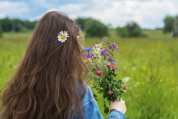 Unrecognizable young girl standing back to us with beautiful summer bouquet of wildflowers in her hands. With place for your text