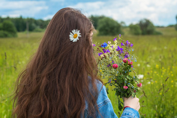 Naklejka premium Young girl with daisie in hair and with beautiful summer bouquet of wild flowers in hand. Concept of seasons, environment, natural beauty, summer hobbies, leisure, lifestyle vacation