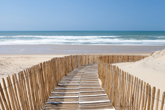 Holzweg mit Zaun verläuft in Kurve durch Dünen zum Strand, Atlantikküste