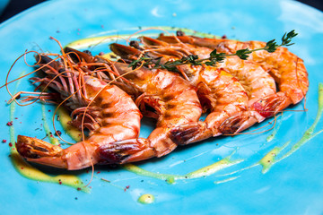 Grilled shrimps with rosemary on the blue plate served in restaurant with sous and wine