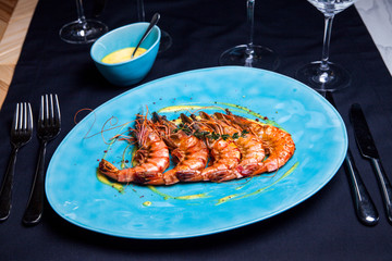 Grilled shrimps with rosemary on the blue plate served in restaurant with sous and wine