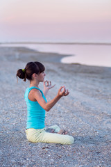 Fototapeta na wymiar Beautiful teen girl doing yoga exercise lotus pose on the background of the sea at sunset