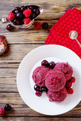 Summer cold refreshing dessert, ice cream, berry sorbet in balls with cherry and raspberries on a dark wooden background