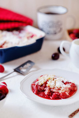 Delicious and juicy berry dessert, pie, coconut Crumble with strawberries, cherry, raspberries, black coffee and milk on a light background