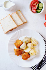Delicious and hearty dinner, chicken balls in breading, with potatoes on a garnish with fresh tomato and cucumber, white toast, olive oil, black coffee and milk on a white background