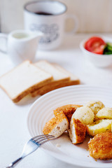 Delicious and hearty dinner, chicken balls in breading, with potatoes on a garnish with fresh tomato and cucumber, white toast, olive oil, black coffee and milk on a white background