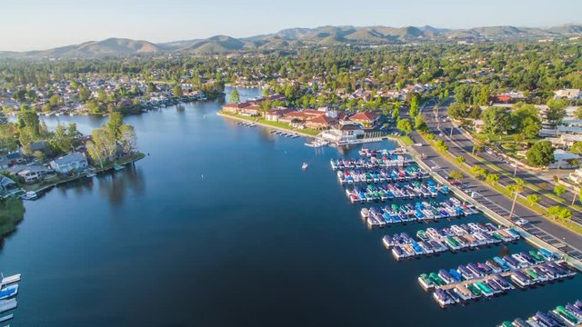 Aerial timelapse in motion (hyperlapse) over the Westlake Village lake with boats, luxury homes, trees, traffic, mountains and blue sunny skies in the background.