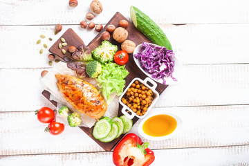 The baked chicken fillet and vegetables. Healthy and fitness food. Meat, salad, vegetables, nuts, beans on a light wooden background. Selective focus. Copy space. Top view