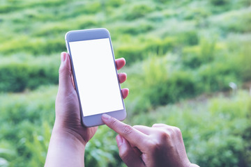 Mockup image of a hand holding , pressing and using white smart phone with blank screen at outdoor and green nature background