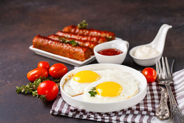 Breakfast - Fried eggs and meat sausages and sauces against a dark background. Selective focus. Copy space