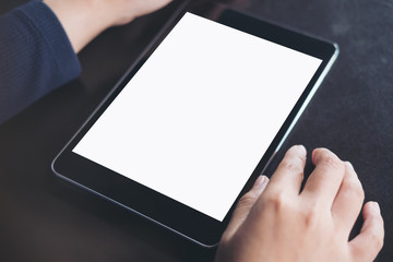Mockup image of hands using a black tablet pc with blank white screen on vintage black table background