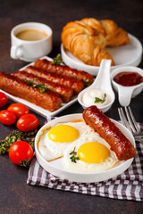 Breakfast - Fried eggs and meat sausages and sauces against a dark background. Selective focus. Copy space