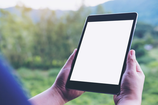 Mockup image of woman's hands holding black tablet pc with blank white screen and green nature background